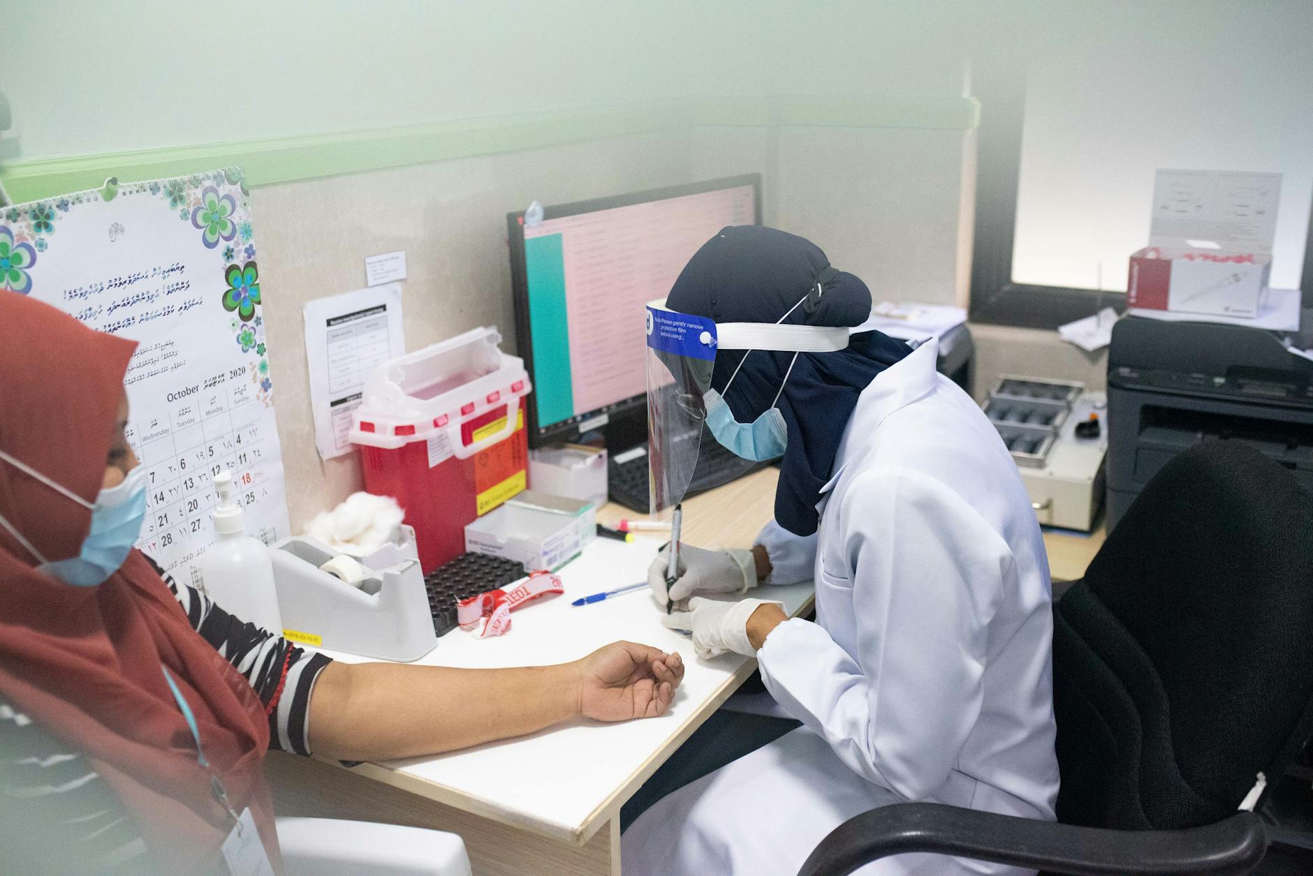 Healthcare worker wearing PPE draws blood from a patient in a clinical setting.